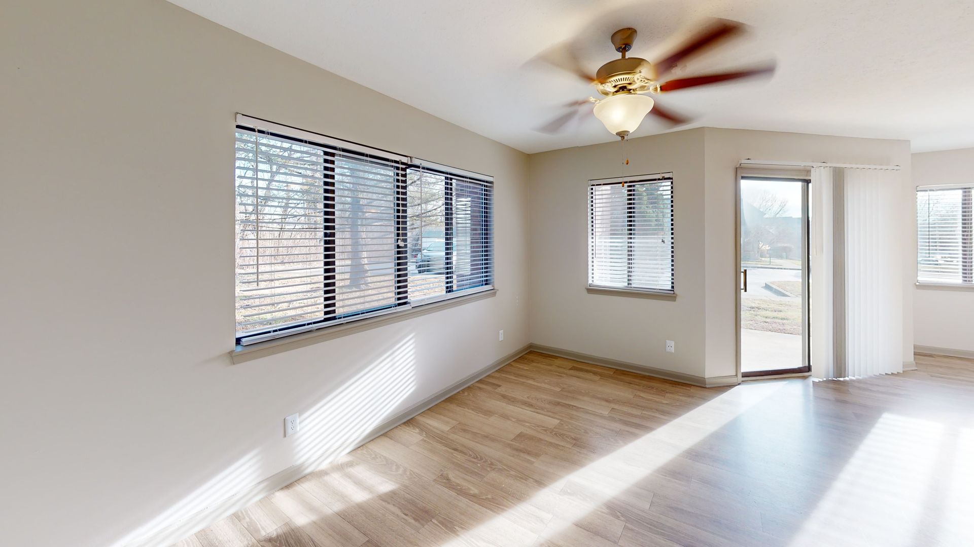 Large living room with plank flooring, a fan, and large windows