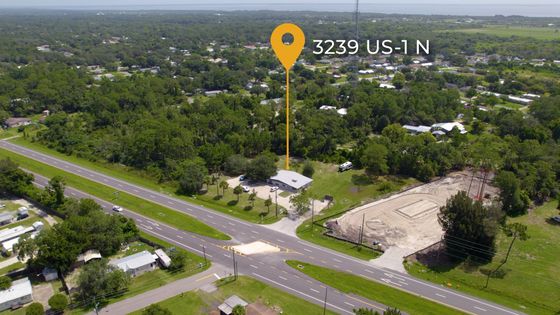 Aerial view of a roadside lot at 3239 U.S. 1, with trees, a building, and nearby open land.
