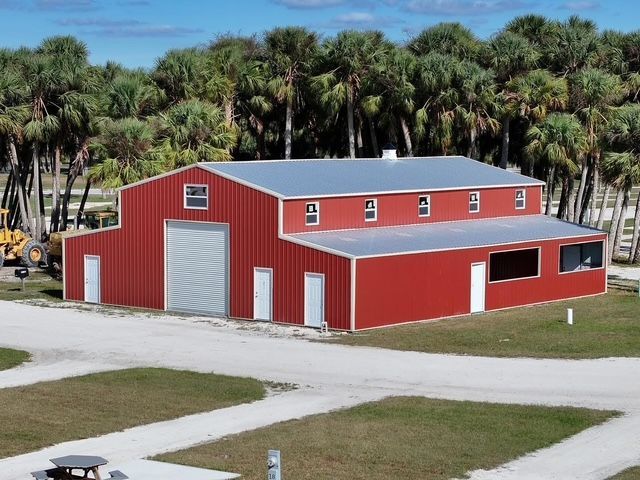 Red metal barn with white trim and a large garage door, set beside a road and palm trees.