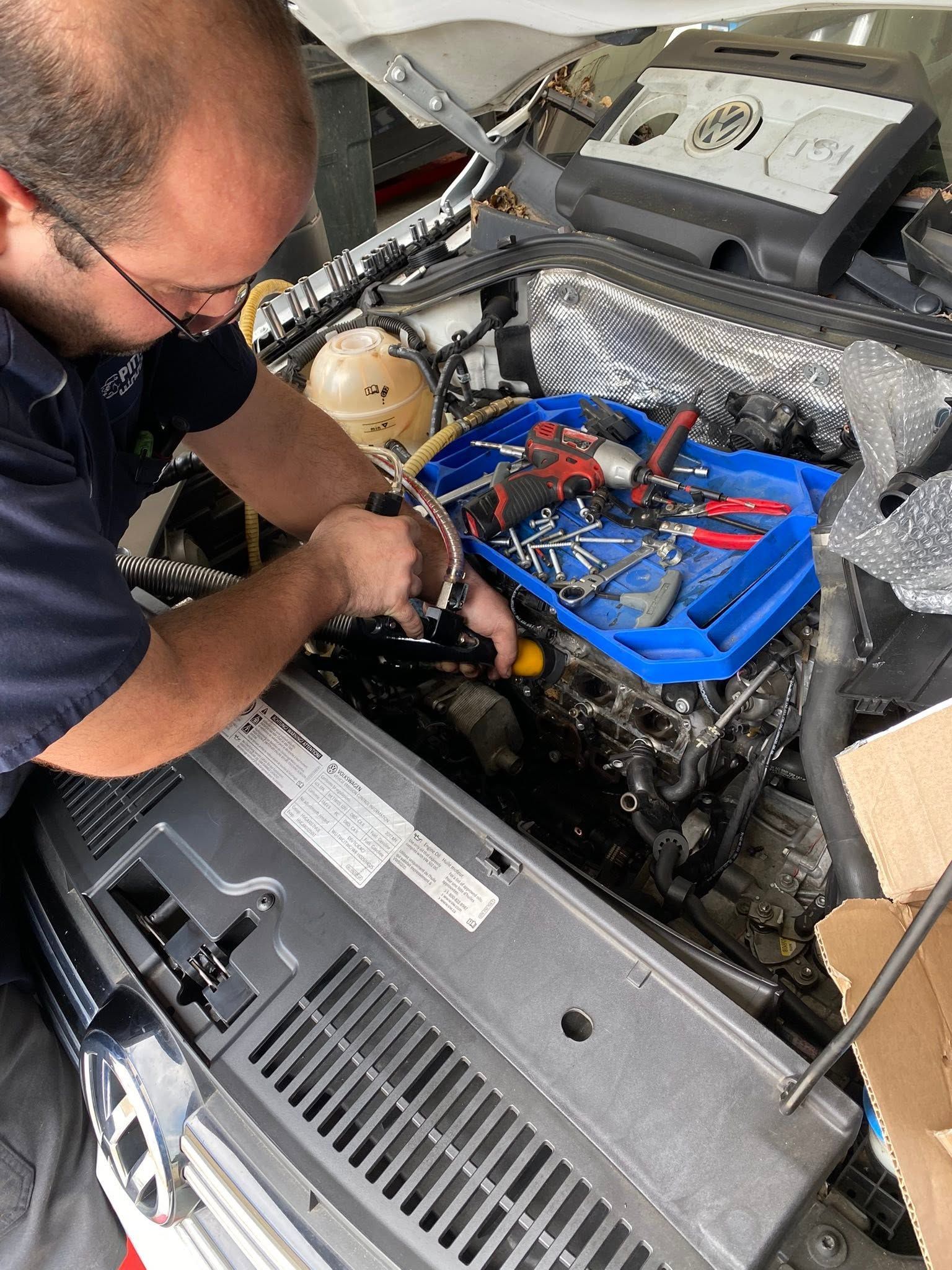 Mechanic working under an open car hood beside blue tool trays and a covered engine area | Pitts Automotive