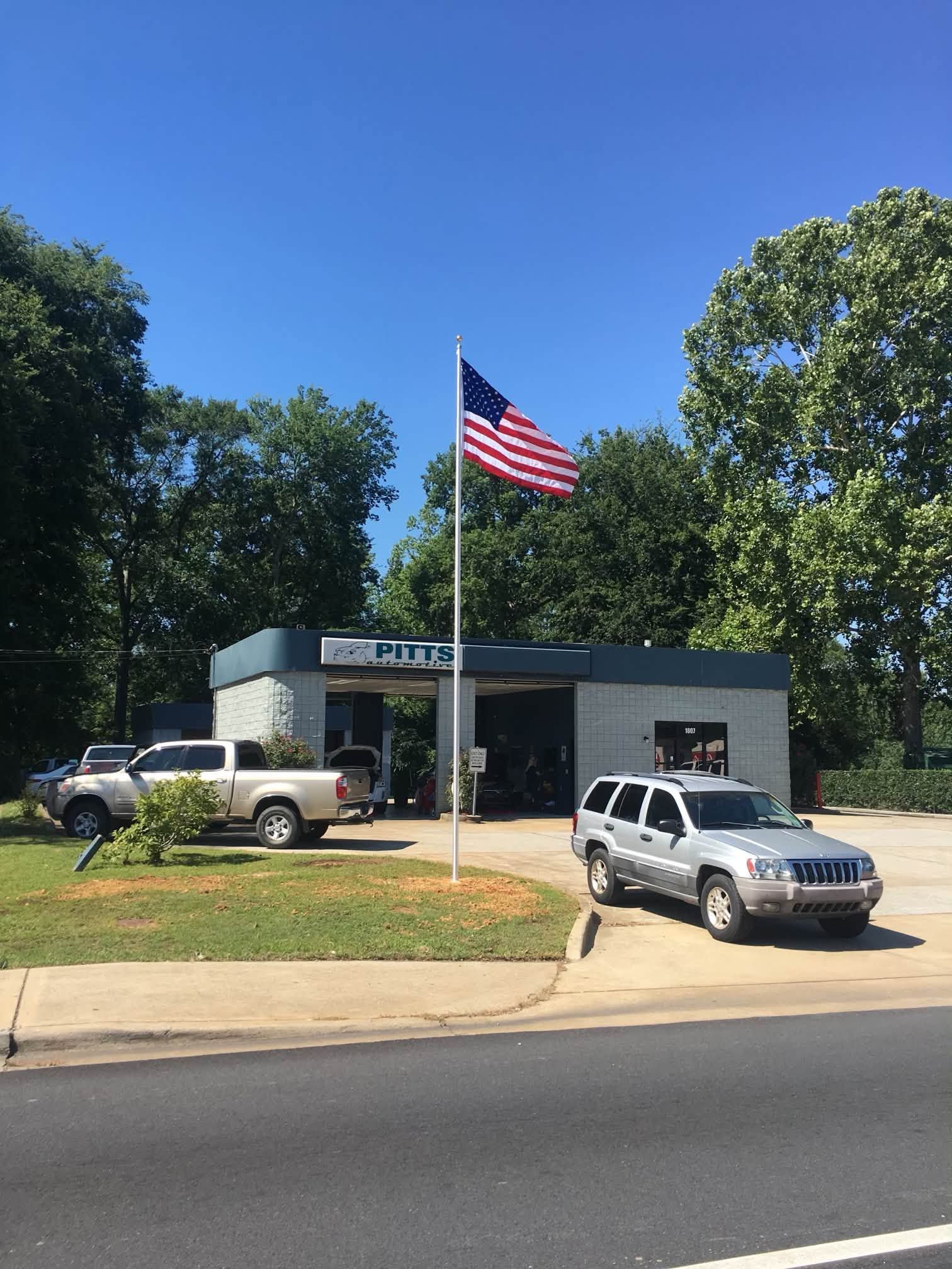 Auto Shop with two parked SUVs and a large American flag flying outside on a sunny day | Pitts Automotive