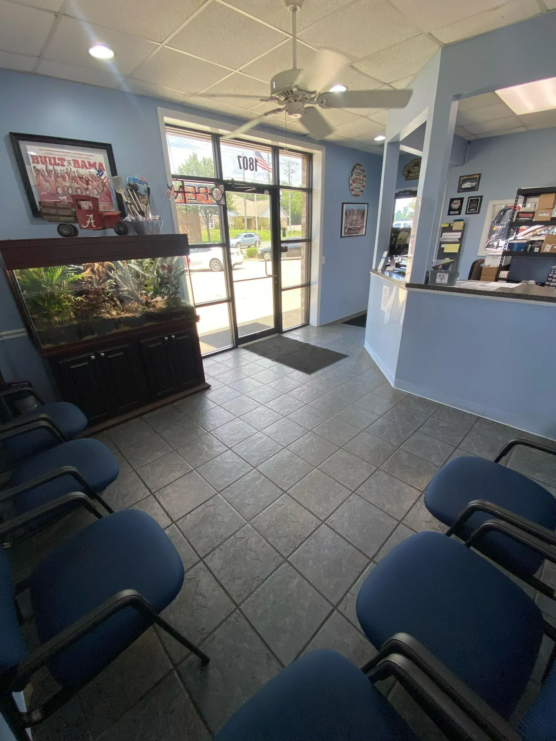 Waiting area with blue chairs, a fish tank, and a glass entrance door in a small office lobby. | Pitts Automotive