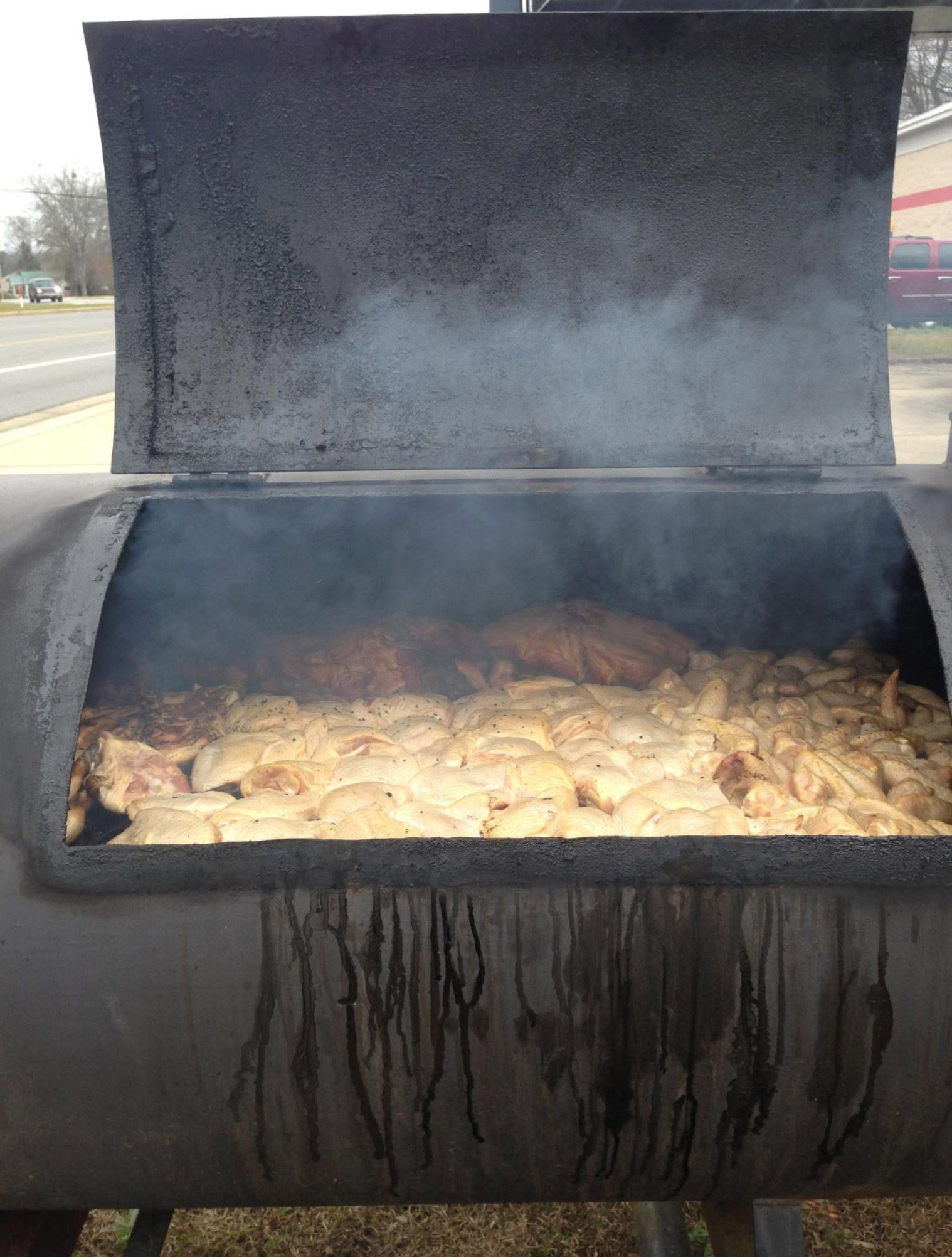 Open smoker grill with several pieces of meat cooking inside, smoke rising from the lid. | Pitts Automotive
