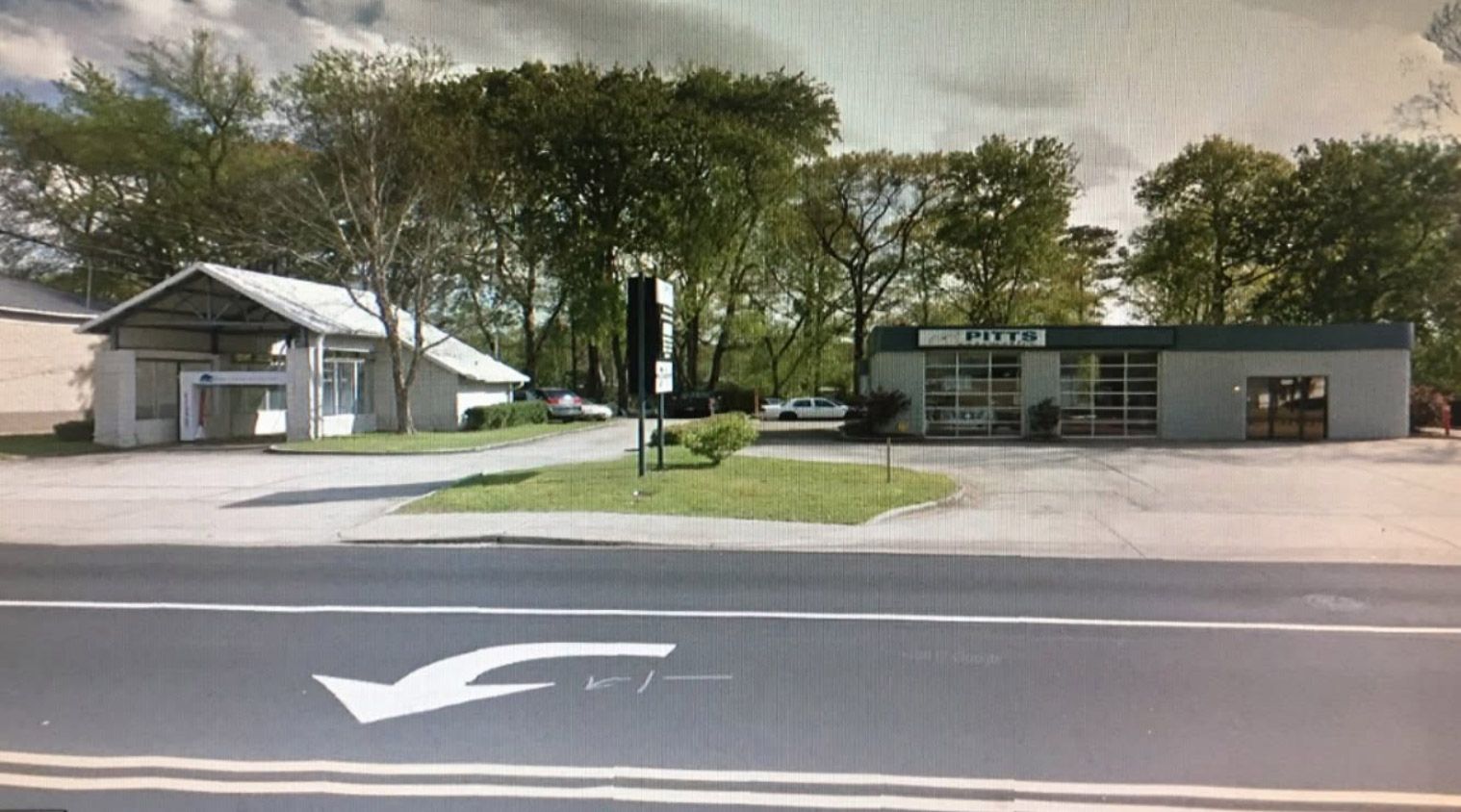 Roadside buildings with trees and a parking lot under a cloudy sky | Pitts Automotive