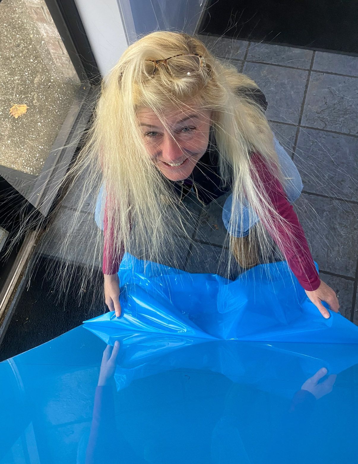 Smiling woman holding a large bright blue sheet indoors by a window | Pitts Automotive