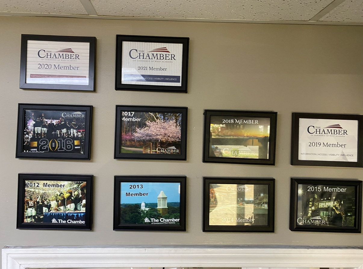 Wall with framed certificates and photos arranged in a grid above a ledge | Pitts Automotive
