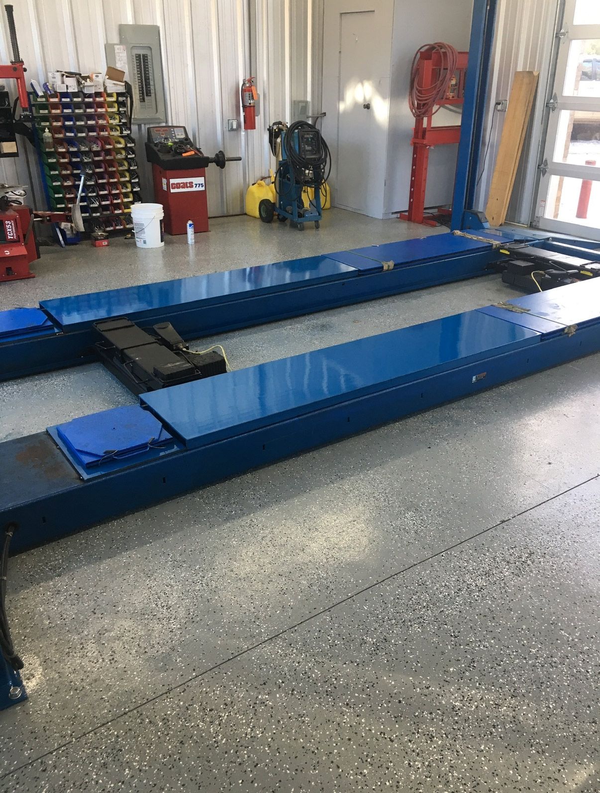 Blue vehicle lift in an auto shop garage with tools and equipment in the background | Pitts Automotive