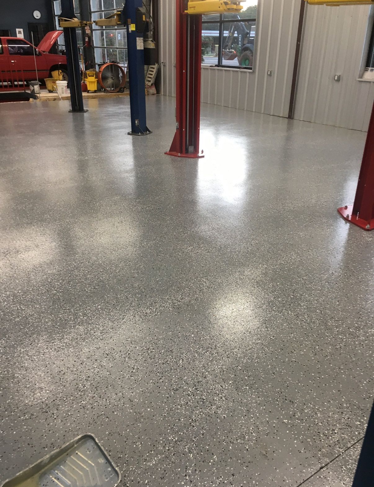 Polished speckled garage floor with red vehicle lift posts and a parked vehicle in the background | Pitts Automotive
