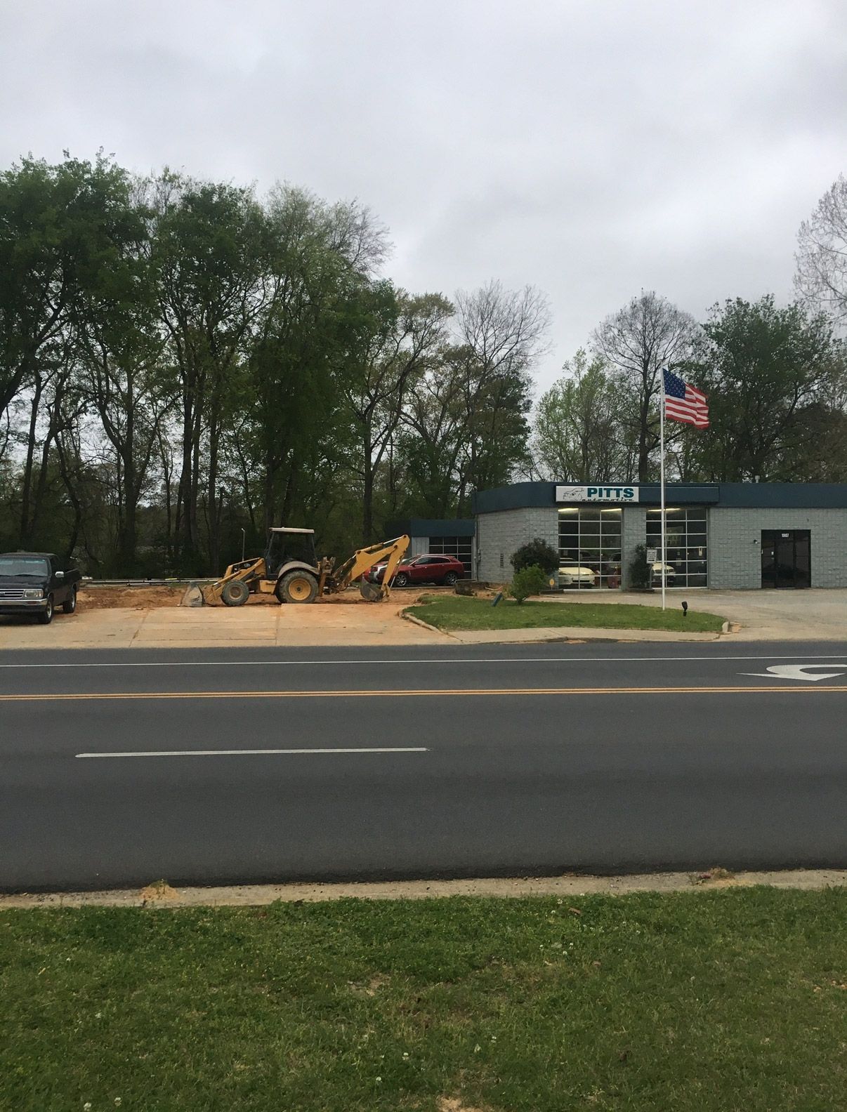 Roadside equipment lot with a small building, parked truck, and trees under a cloudy sky. | Pitts Automotive