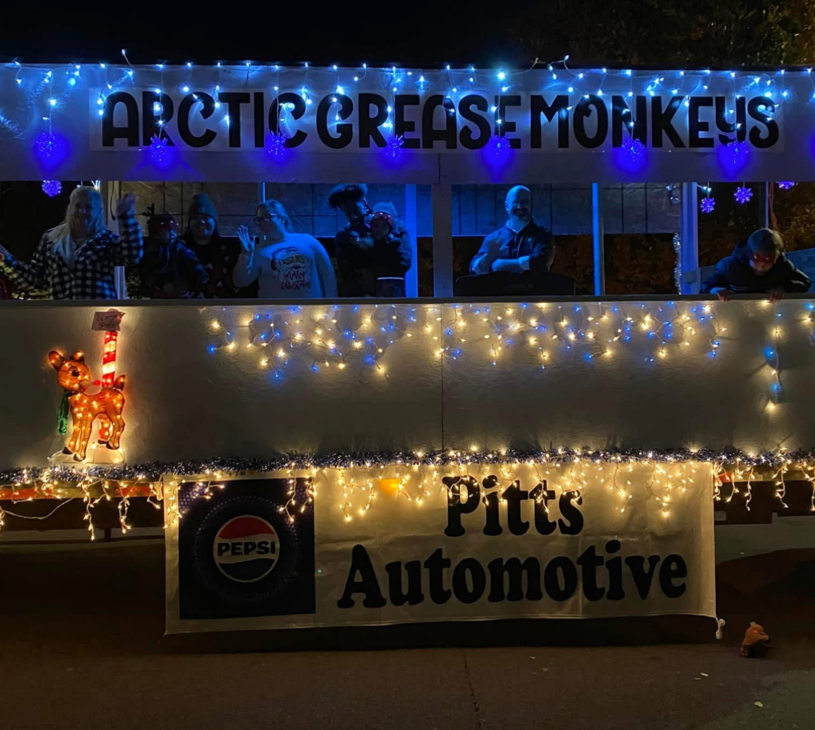 Nighttime storefront with blue-lit “Arctic Creek” sign, string lights, and a “Pitts Automotive” banner.