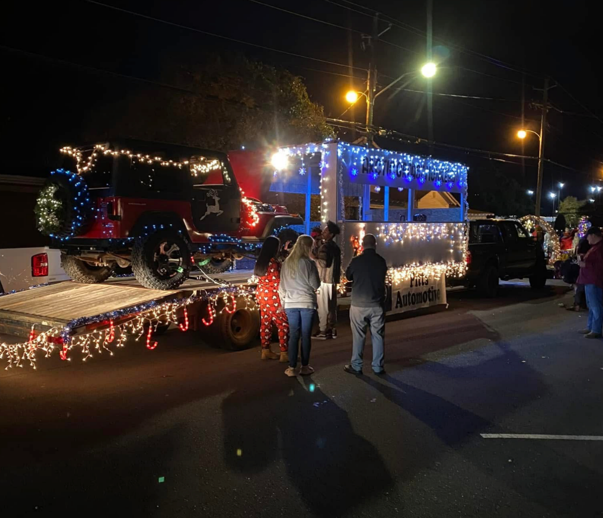 Christmas parade float with blue lights, decorated truck, and people standing beside it at night | Pitts Automotive