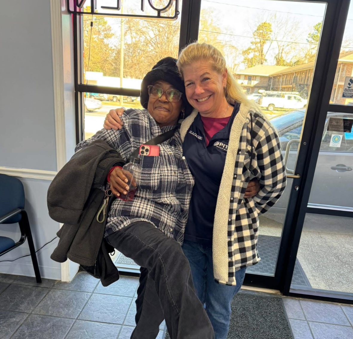 Two people smiling and posing together indoors near a glass door. | Pitts Automotive