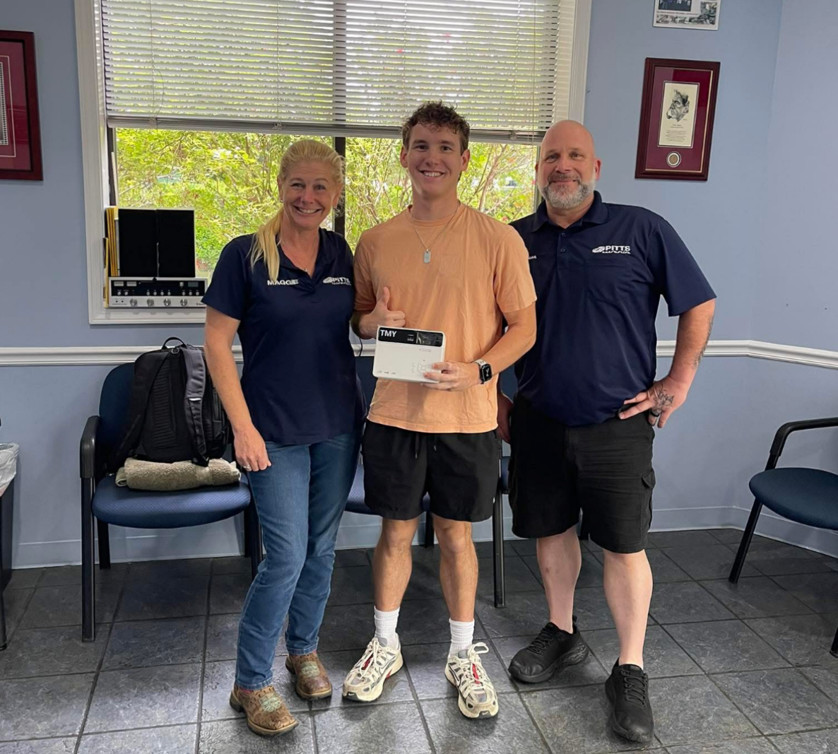 Three people standing indoors, smiling and holding a small award plaque together | Pitts Automotive