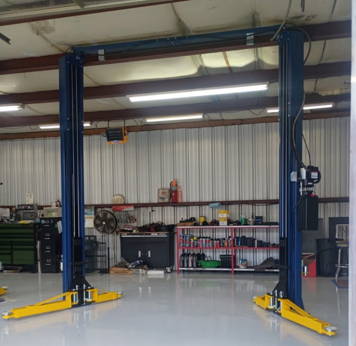 Empty two-post car lift in an auto shop with yellow arms and blue columns | Pitts Automotive