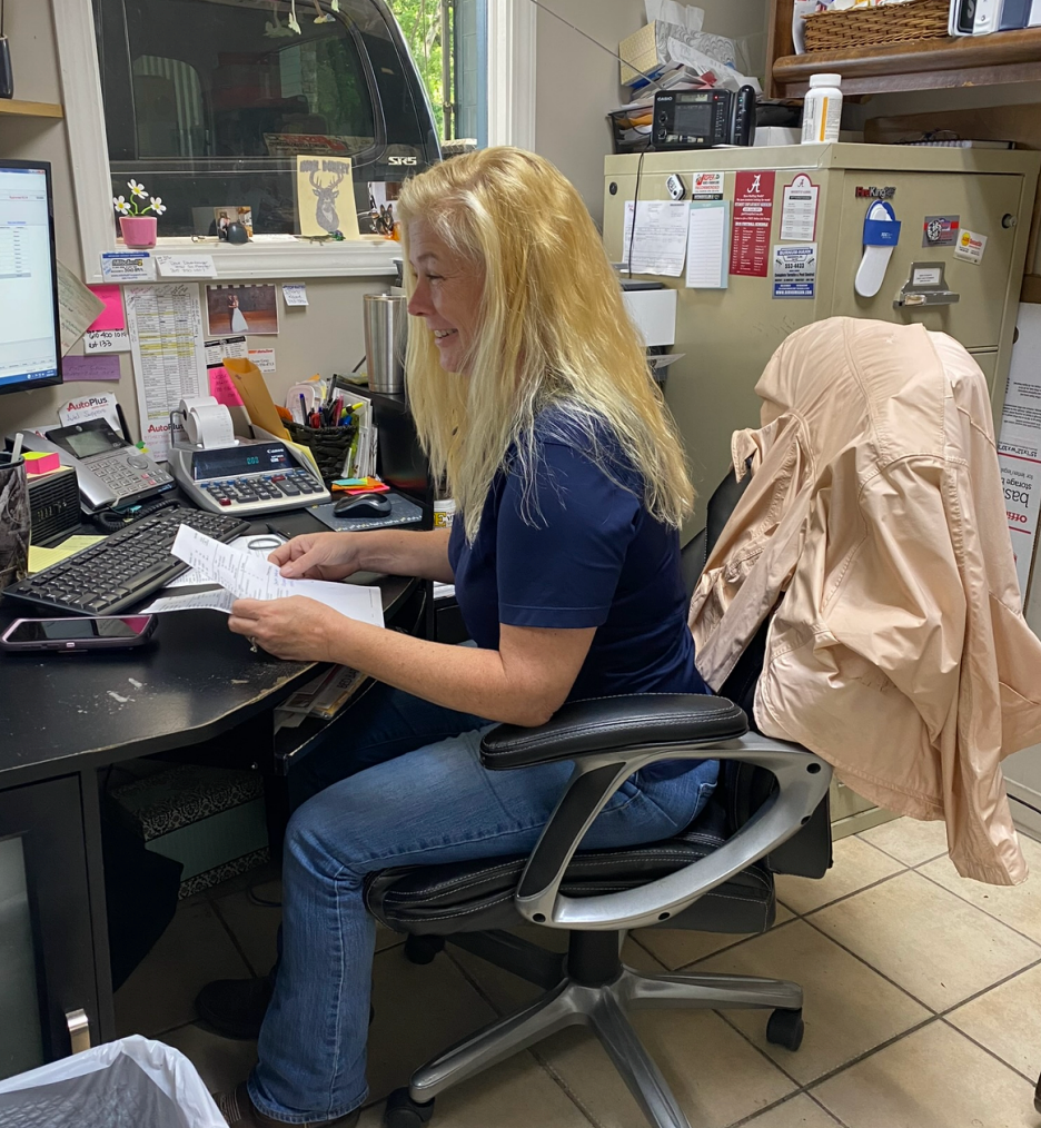 Woman working at a desk in an office, reviewing papers beside a computer and phone. | Pitts Automotive