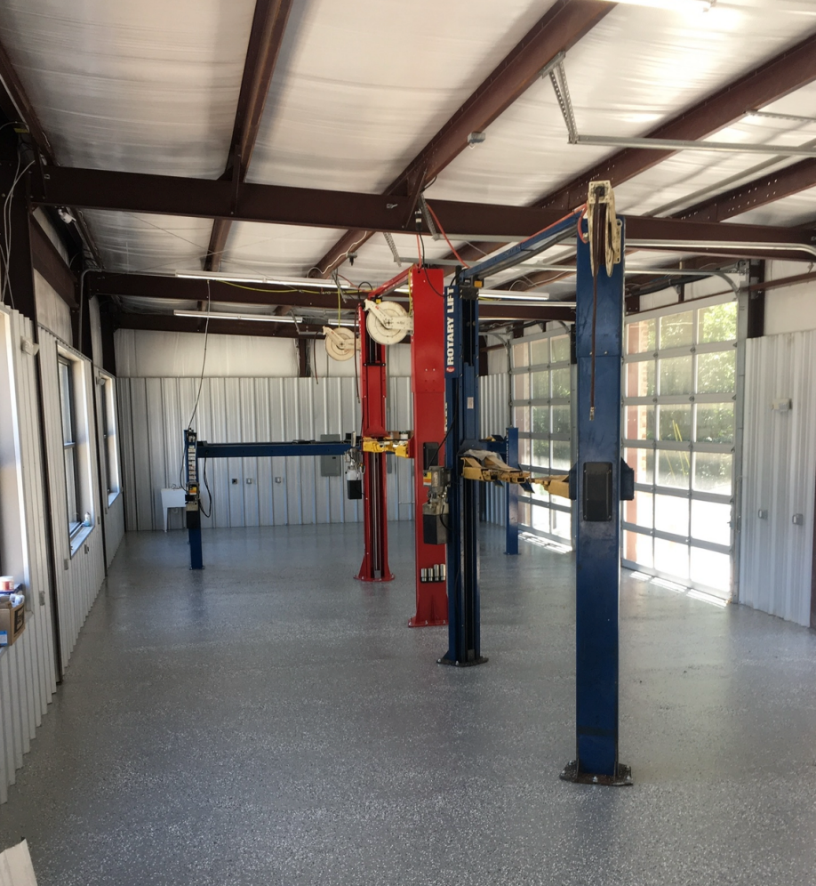 Empty auto shop interior with three vehicle lifts, metal walls, and a polished concrete floor | Pitts Automotive