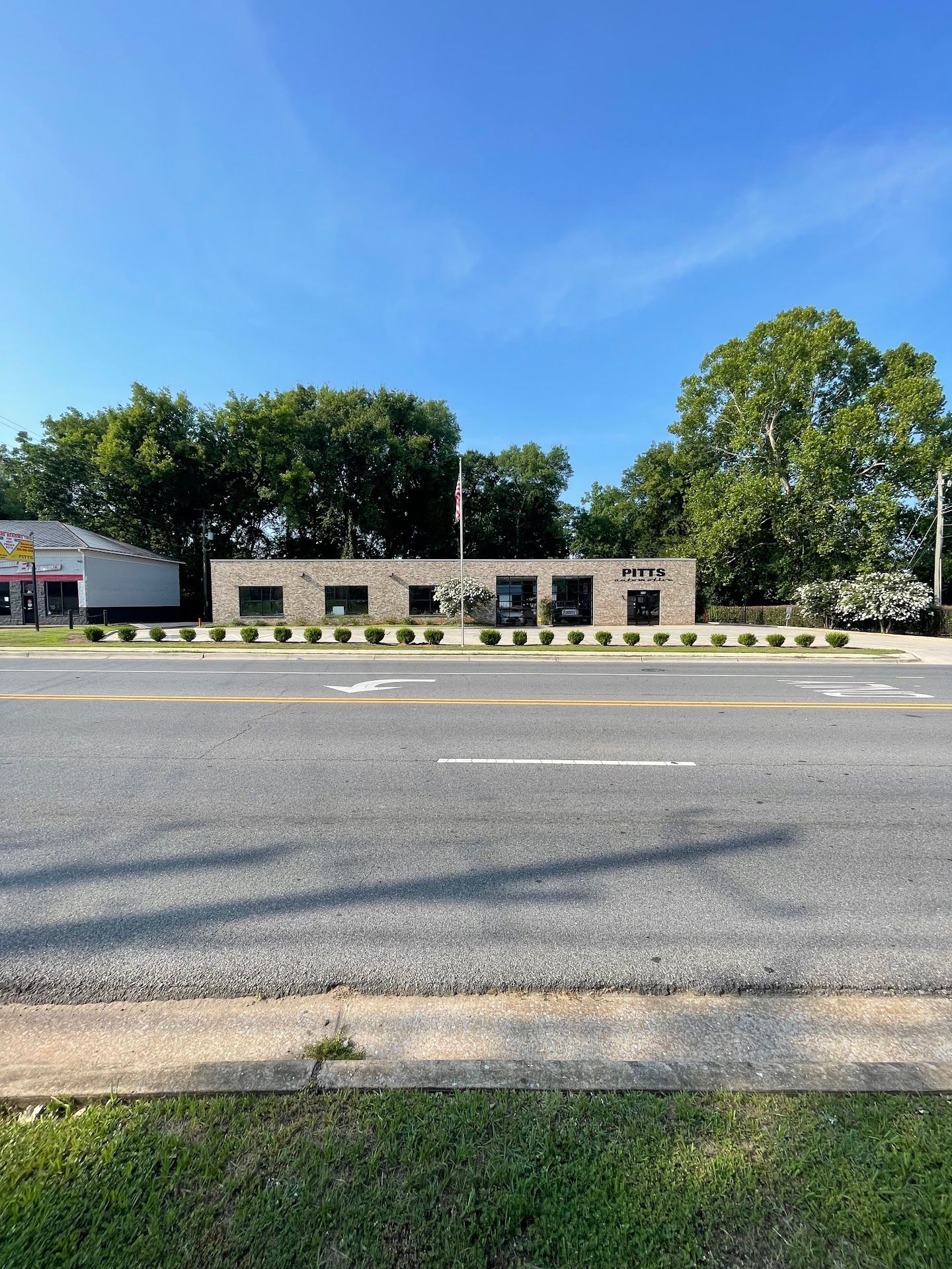 Low brick building with windows behind a road and grass under a clear blue sky | Pitts Automotive
