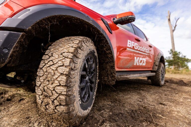 Mud-covered all-terrain tire on a red pickup truck
