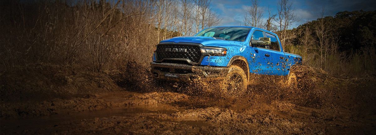 Blue pickup truck splashing through mud on an off-road trail