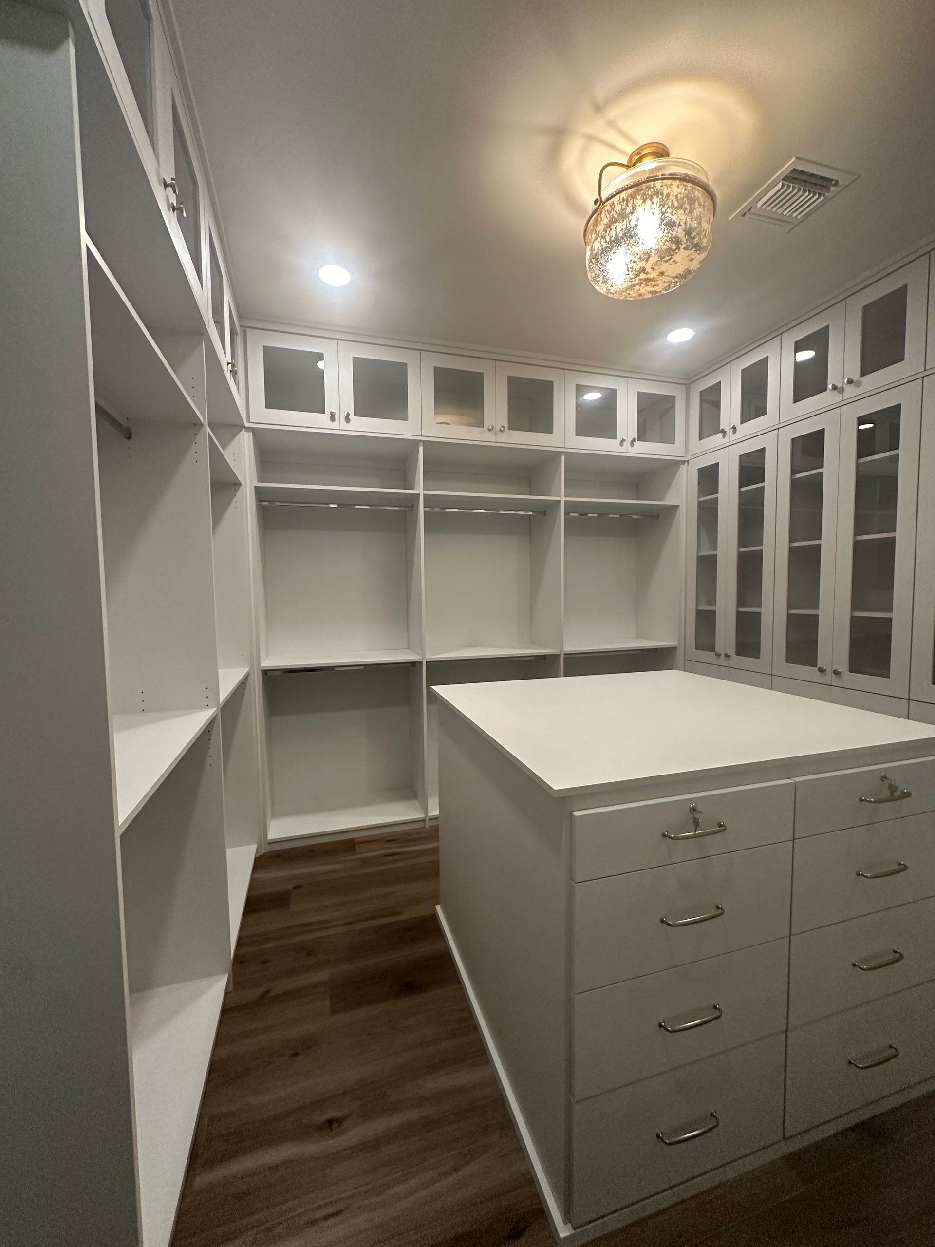 A walk in closet with lots of shelves and drawers and a large island in the middle.