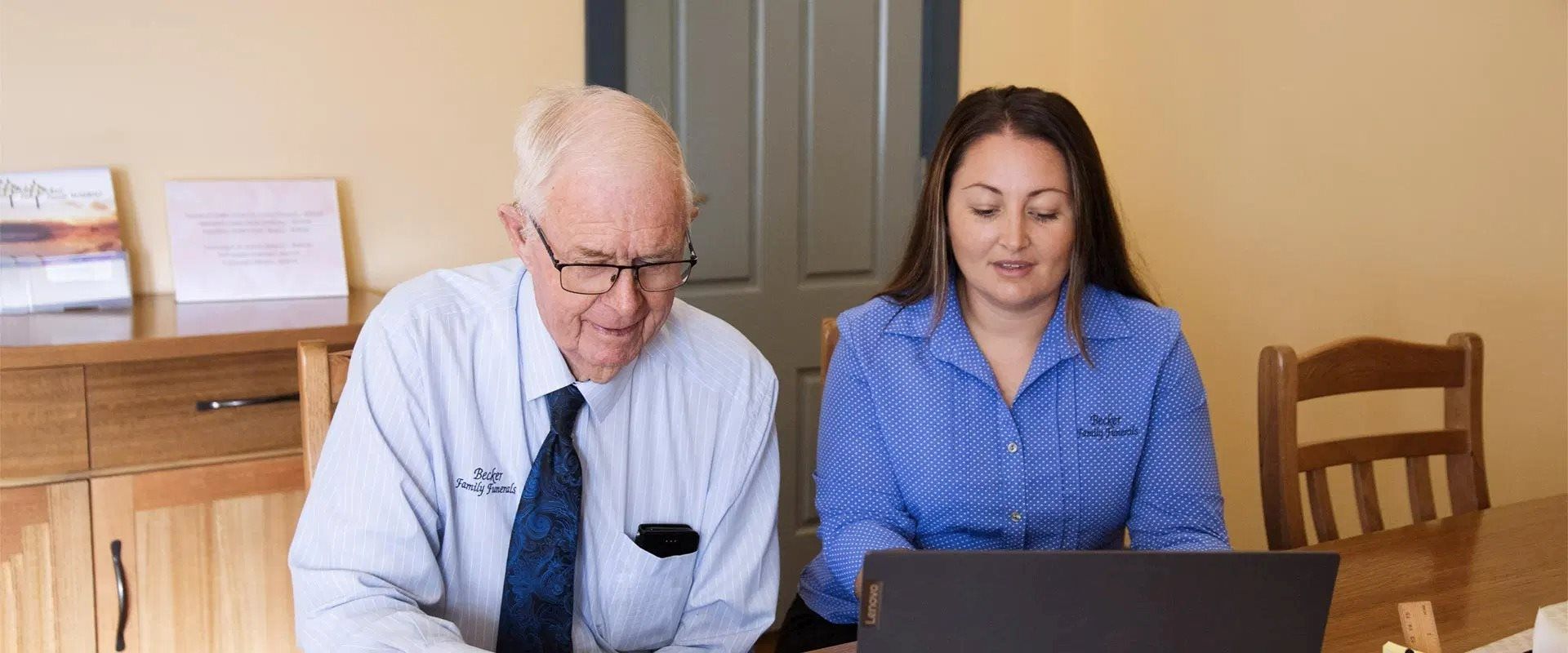 A Man and a Woman Are Sitting at a Table Looking at a Laptop Computer — Becker Family Funerals In Taree, NSW