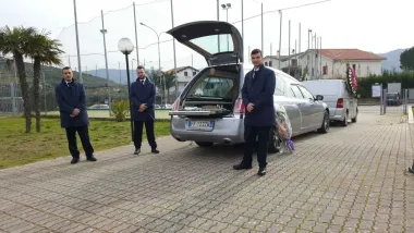 In un parcheggio, tre persone sono in piedi accanto a un'auto argentata con il portellone aperto.