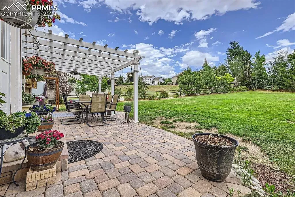 There is a patio with a pergola and a table and chairs on it.