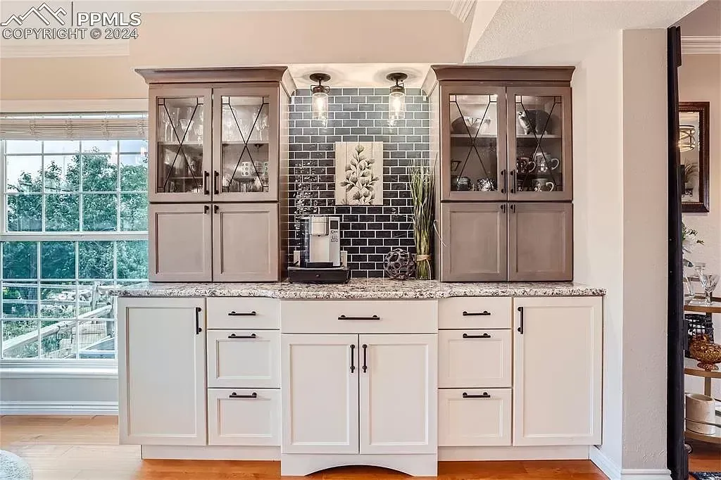 A kitchen with white cabinets , granite counter tops , and a bar.