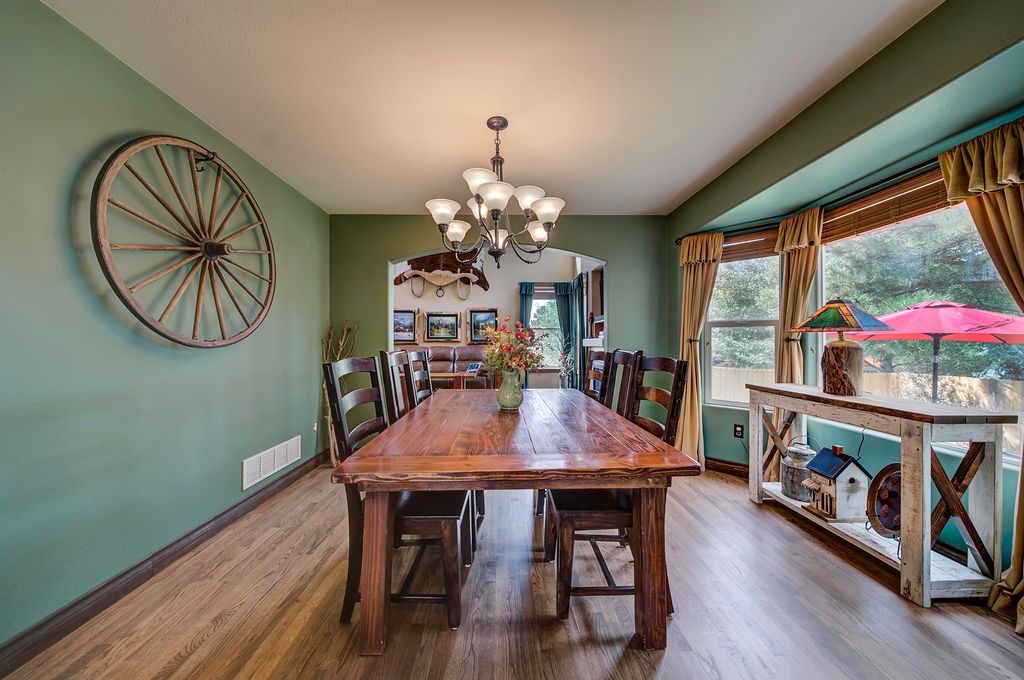A dining room with a wooden table and chairs and a wagon wheel on the wall.