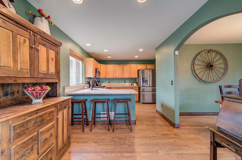 A kitchen with green walls and wooden cabinets and a wagon wheel on the wall.