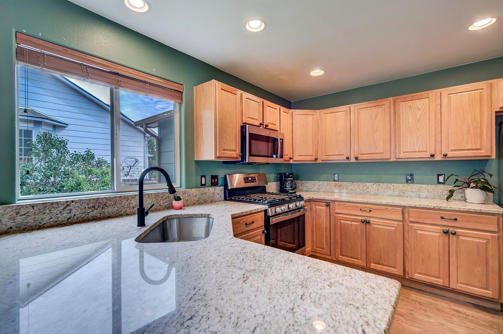 A kitchen with wooden cabinets , granite counter tops , stainless steel appliances and a large window.