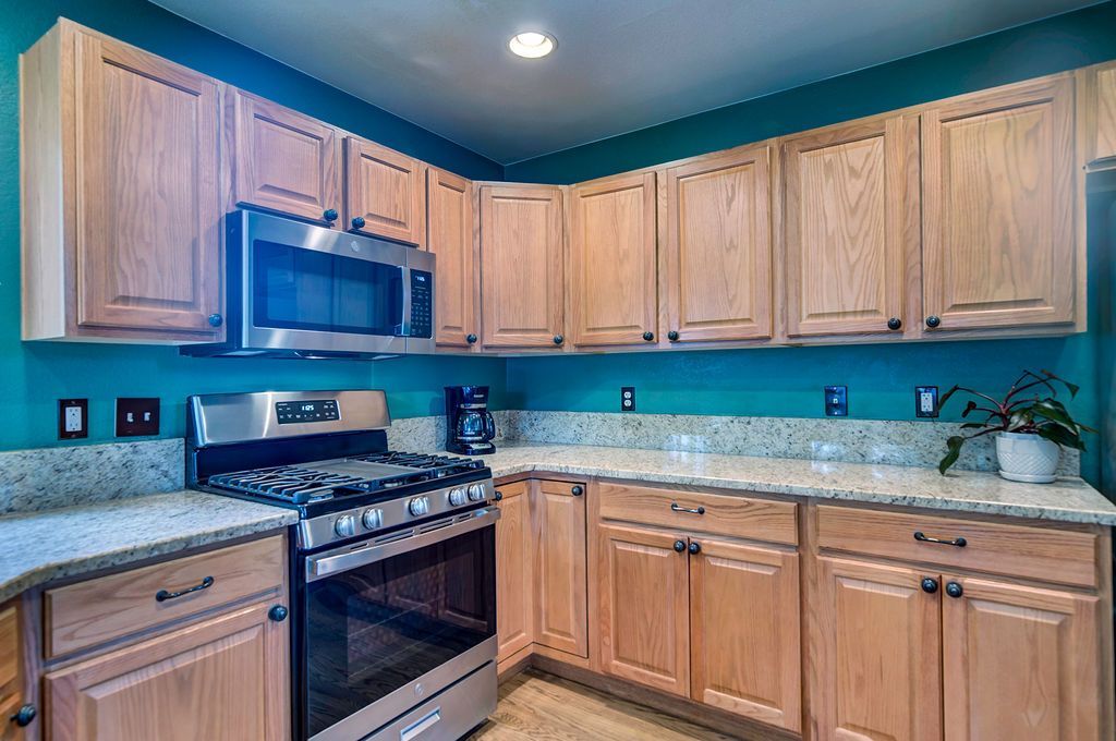 A kitchen with wooden cabinets , stainless steel appliances , granite counter tops and blue walls.