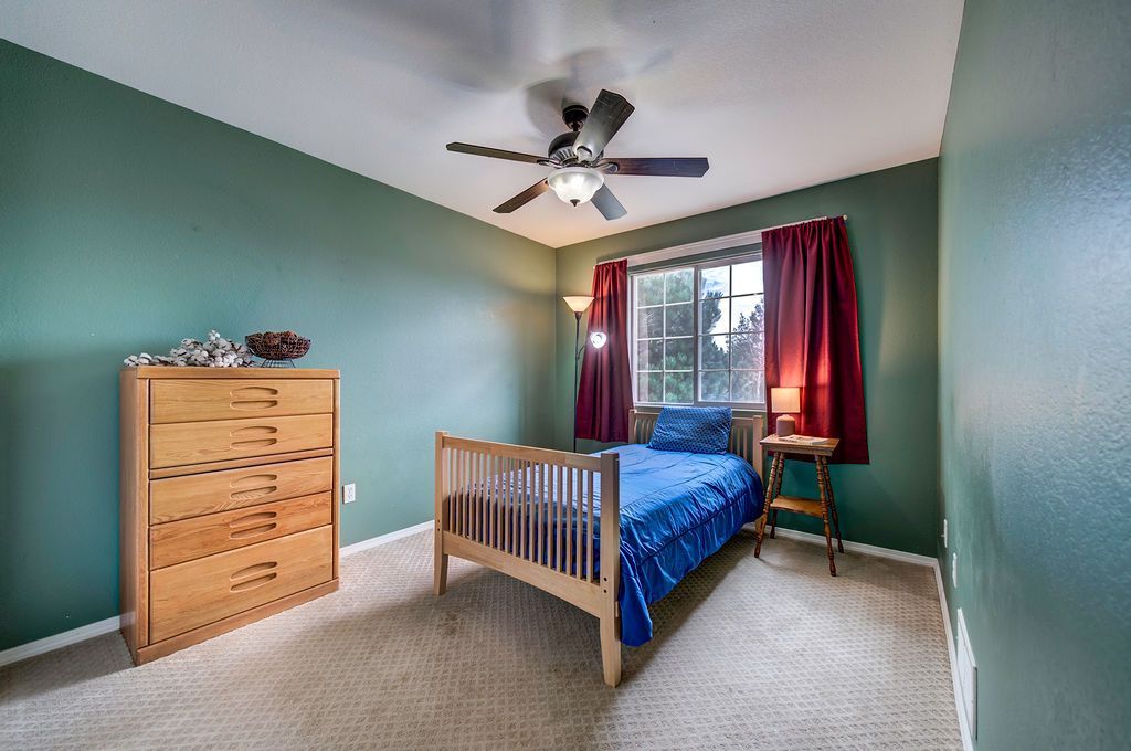 A bedroom with a bed , dresser , and ceiling fan.