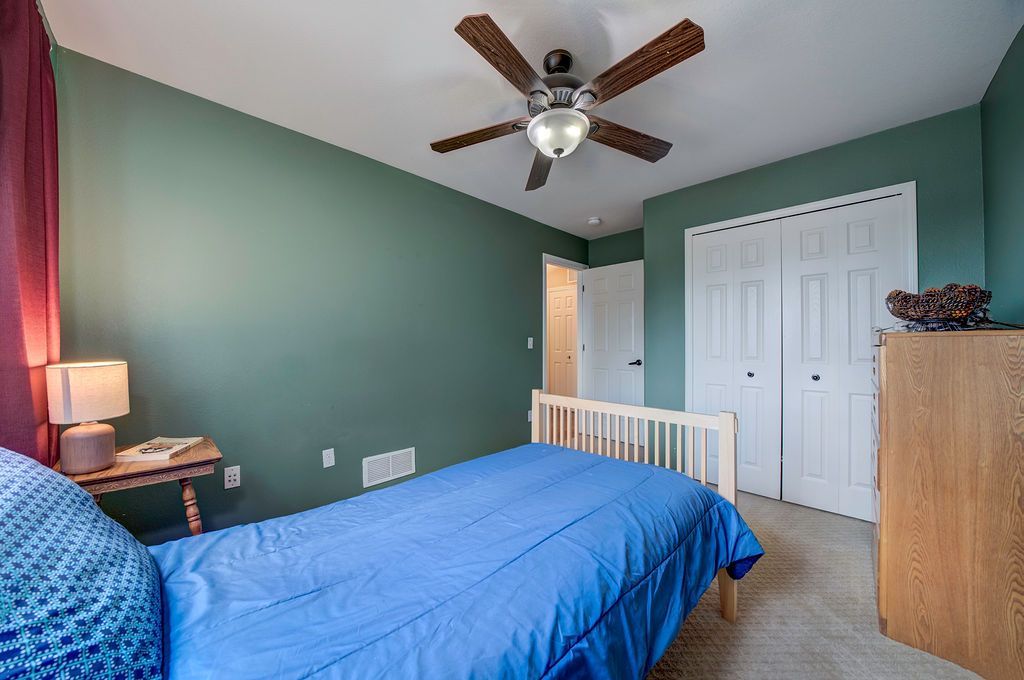 A bedroom with green walls , a blue bed , a ceiling fan and a dresser.