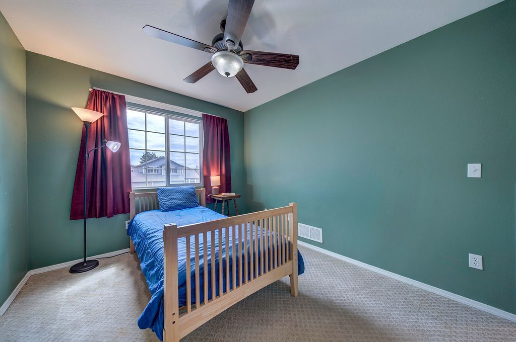 A bedroom with green walls and a bed and a ceiling fan.