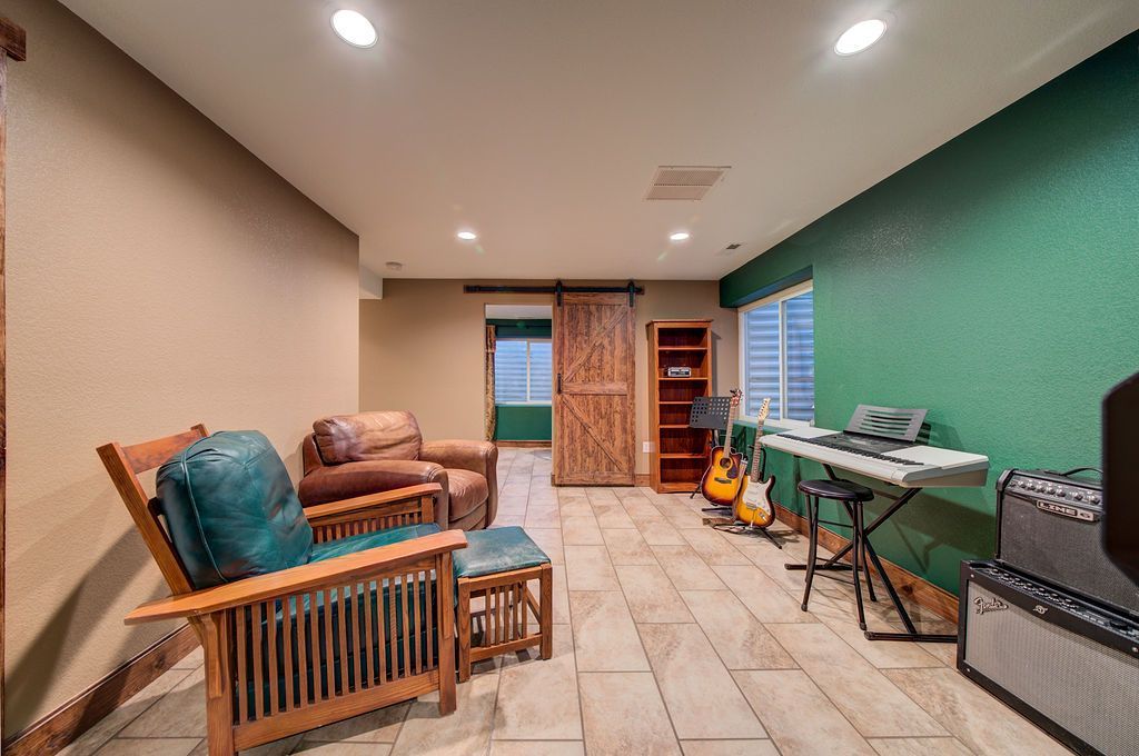 A living room with a sliding barn door , chairs , a keyboard and a guitar.