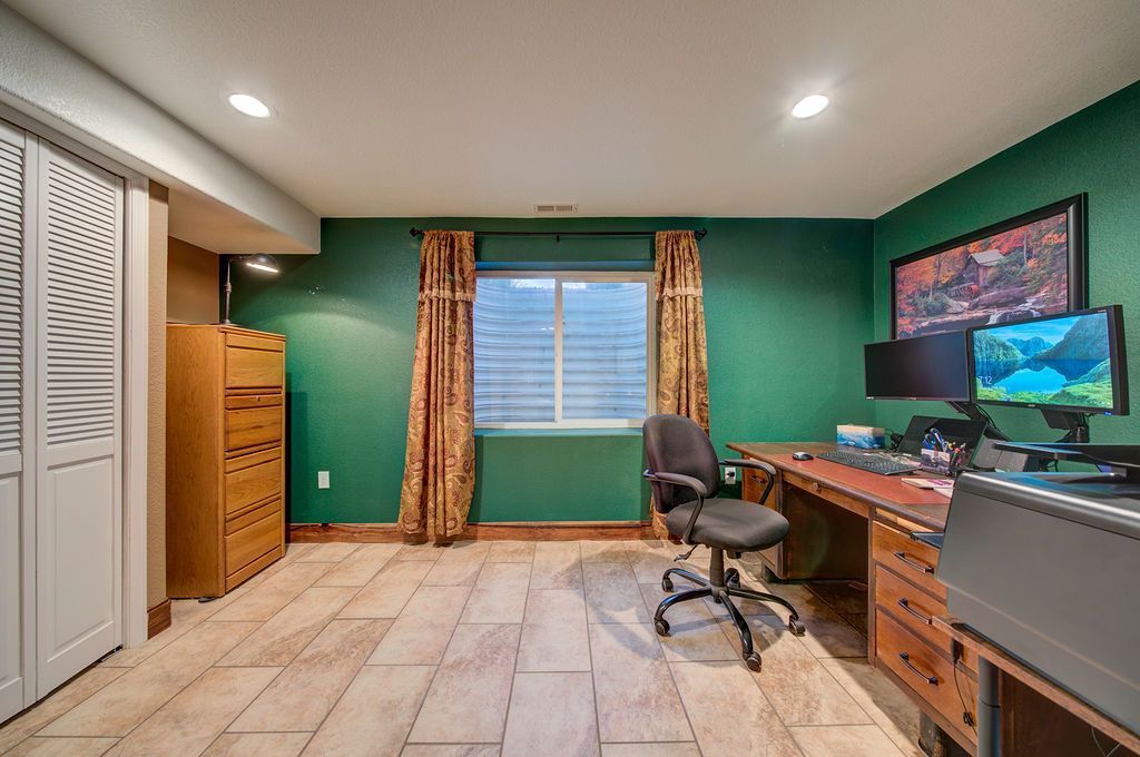 A home office with green walls , a desk , chair , computer monitors and a window.