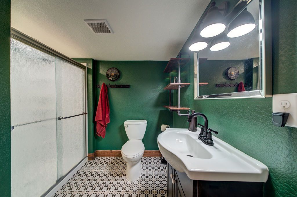 A bathroom with green walls , a toilet , sink and mirror.