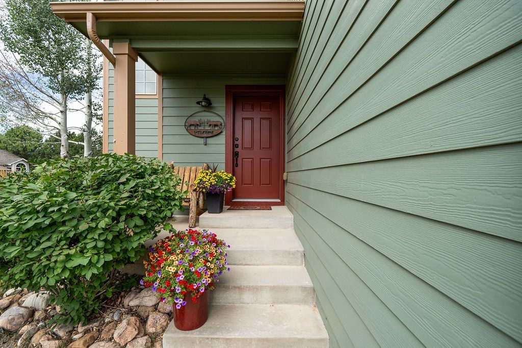 A green house with a red door and flowers in front of it.