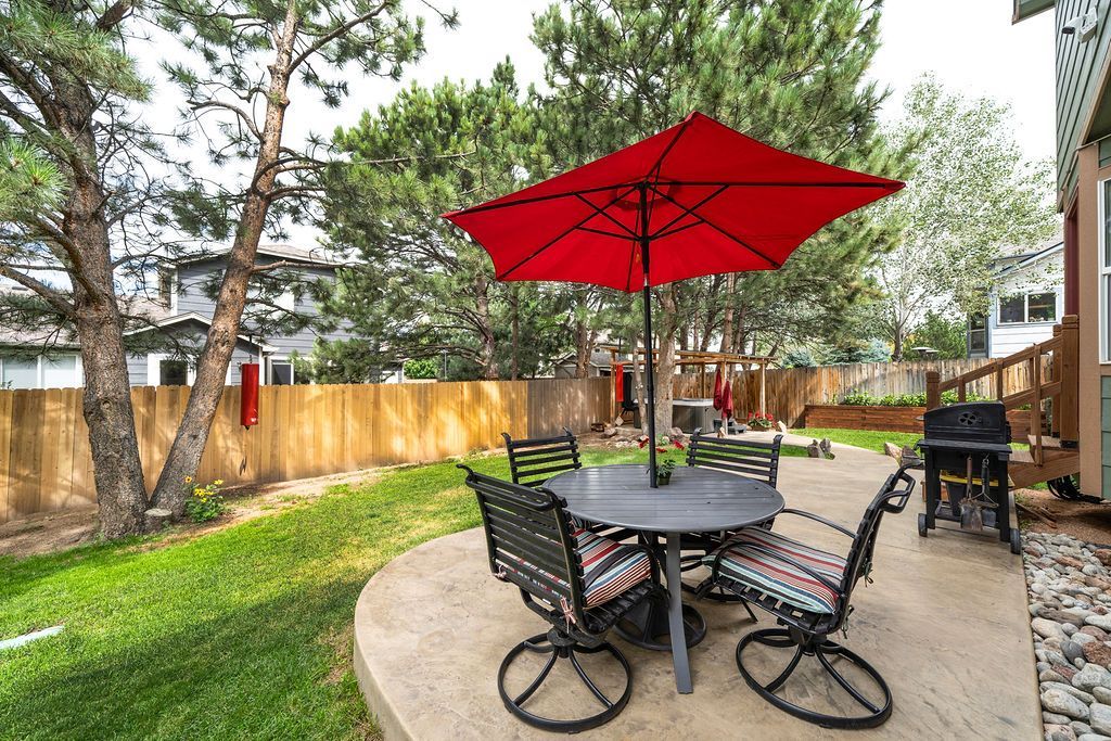 A patio with a table and chairs and a red umbrella.