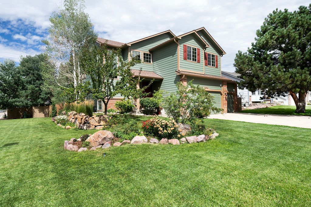A large house with a green roof is surrounded by trees and a lush green lawn.