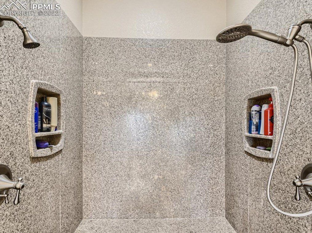 A bathroom with two showers and shelves filled with bottles.