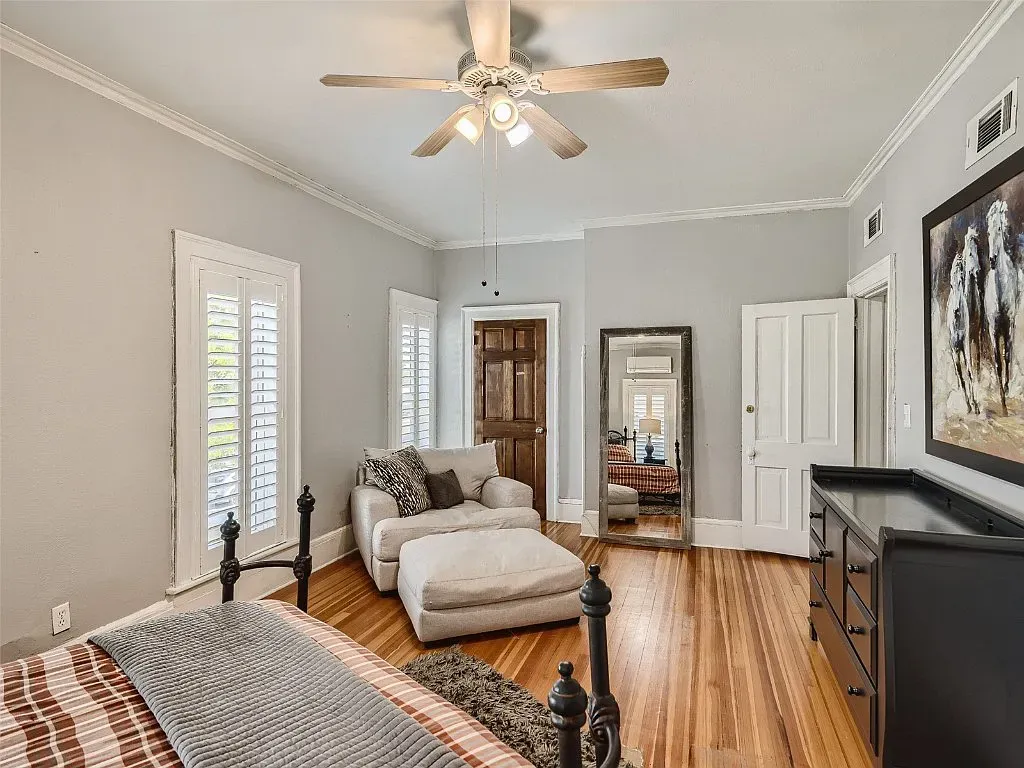 A bedroom with a bed , chair , ottoman and ceiling fan.
