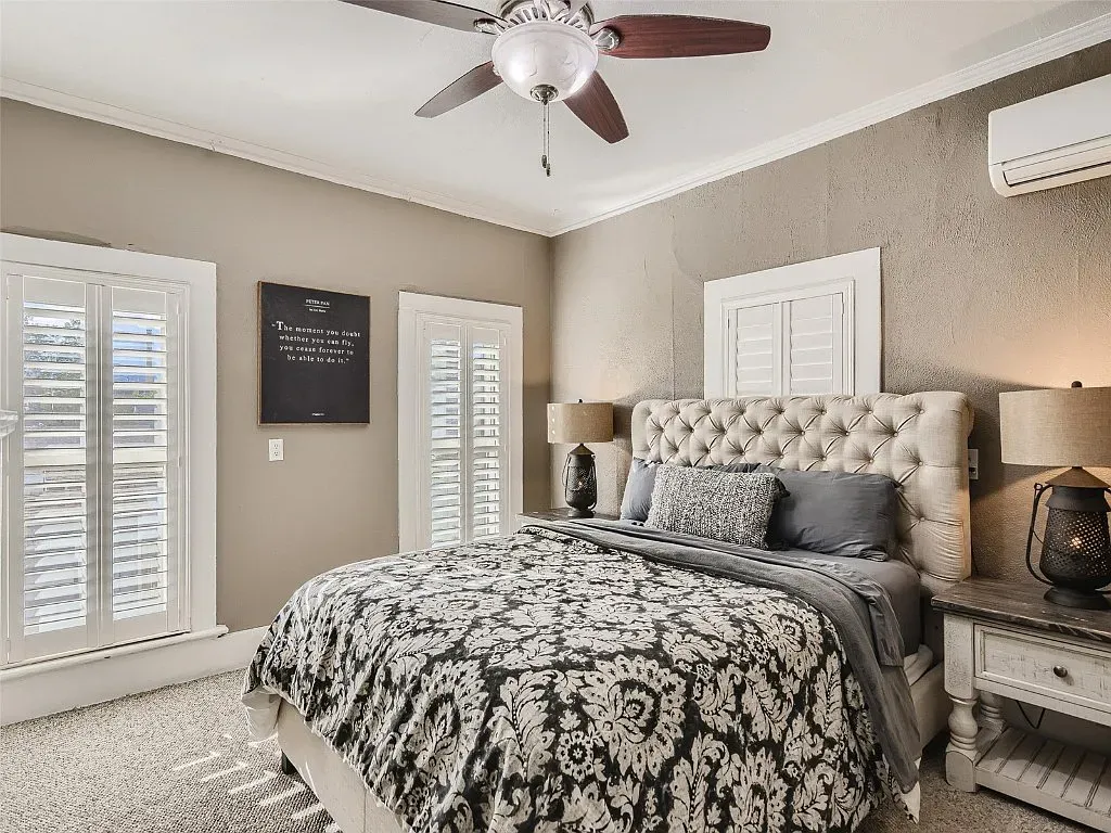 A bedroom with a bed , ceiling fan , lamps and shutters.