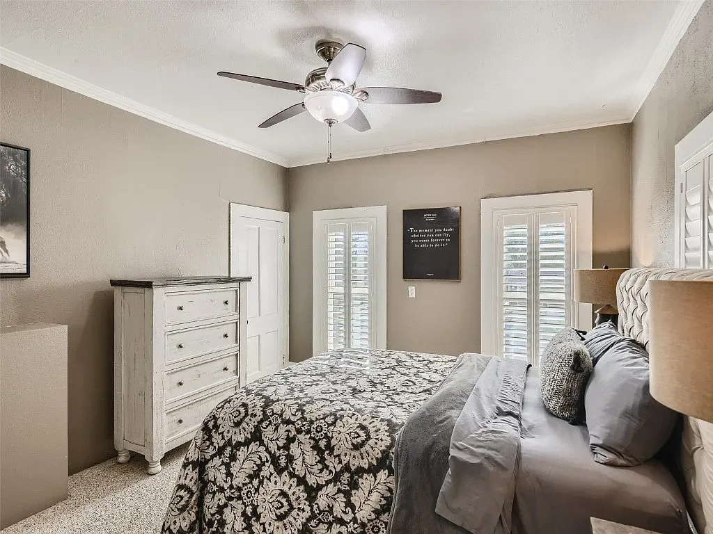 A bedroom with a bed , dresser , lamp and ceiling fan.