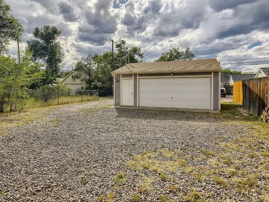 There is a garage in the middle of a gravel driveway.