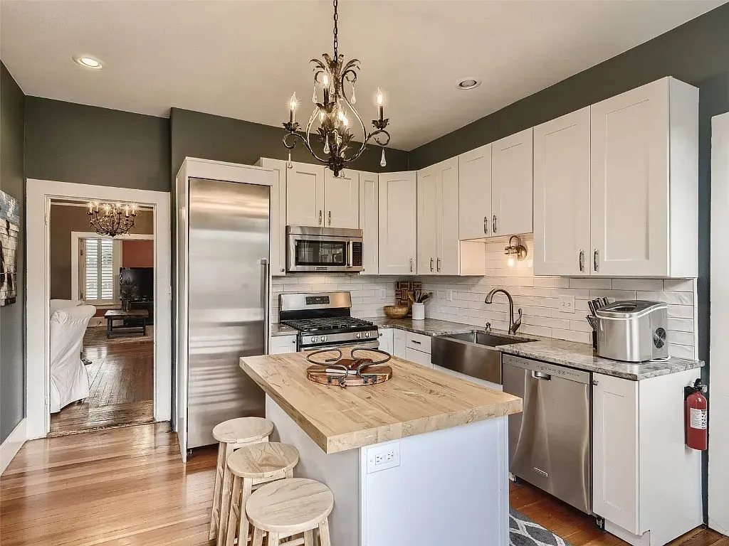 A kitchen with white cabinets , stainless steel appliances , a large island and a chandelier.