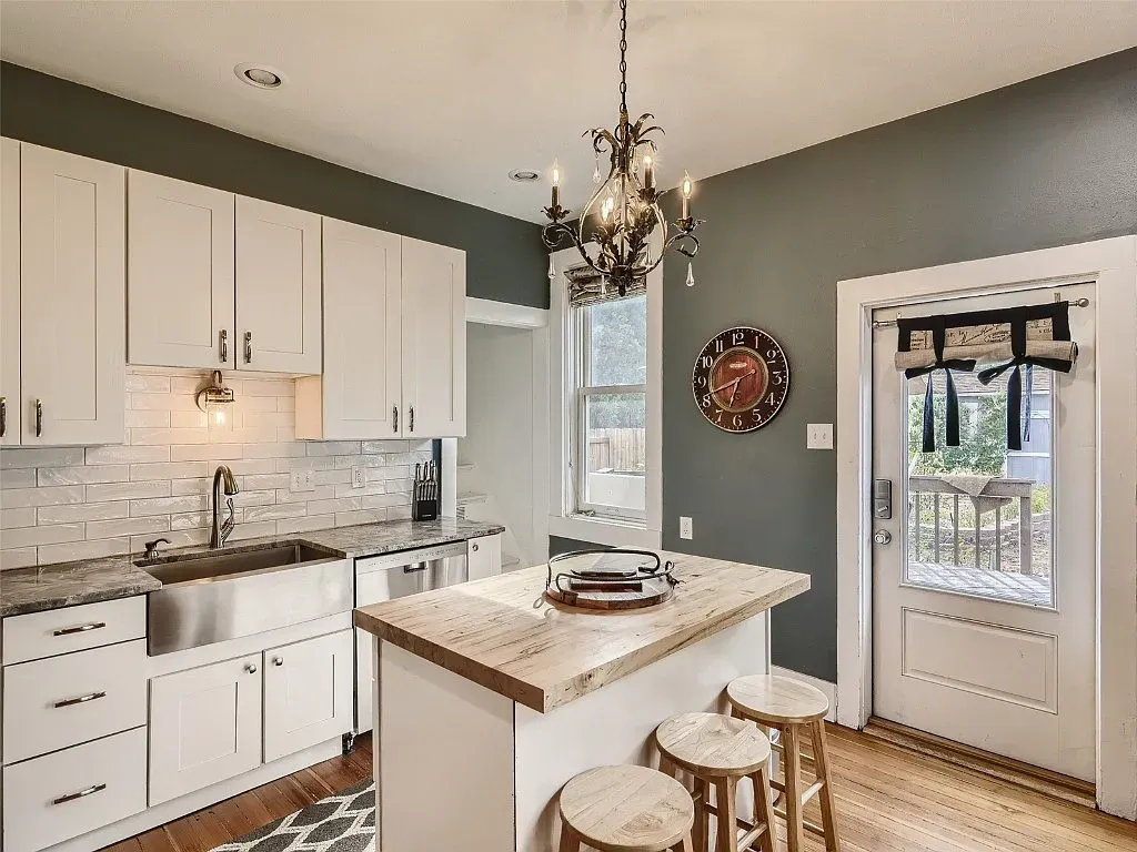 A kitchen with white cabinets , stools , a sink and a chandelier.