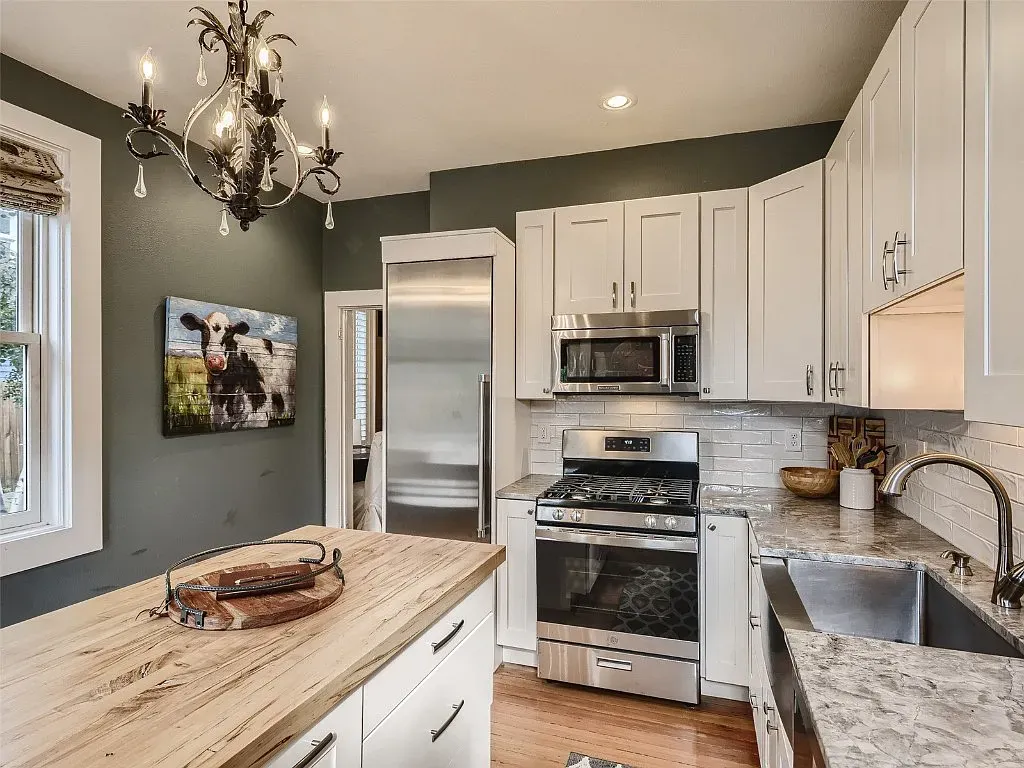 A kitchen with white cabinets , stainless steel appliances , a sink , and a cow painting on the wall.
