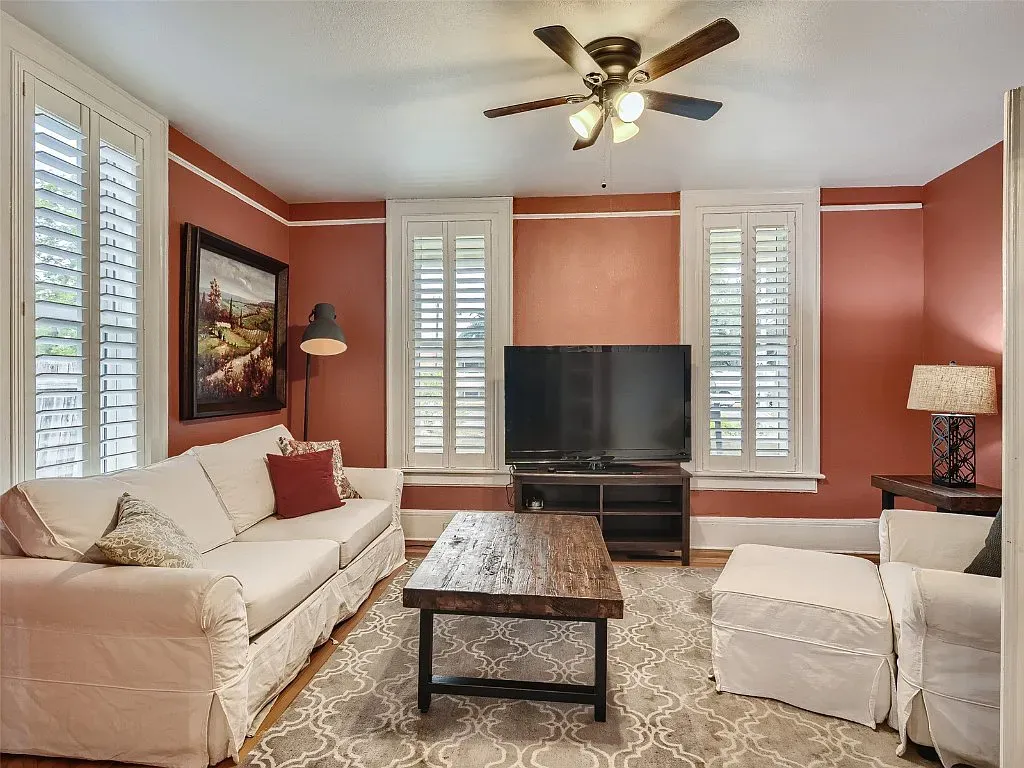 A living room with a couch , chairs , coffee table , television and ceiling fan.